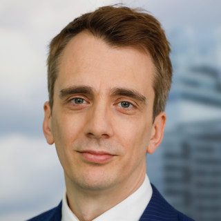 Professional headshot of a man in a suit with a cityscape in the background